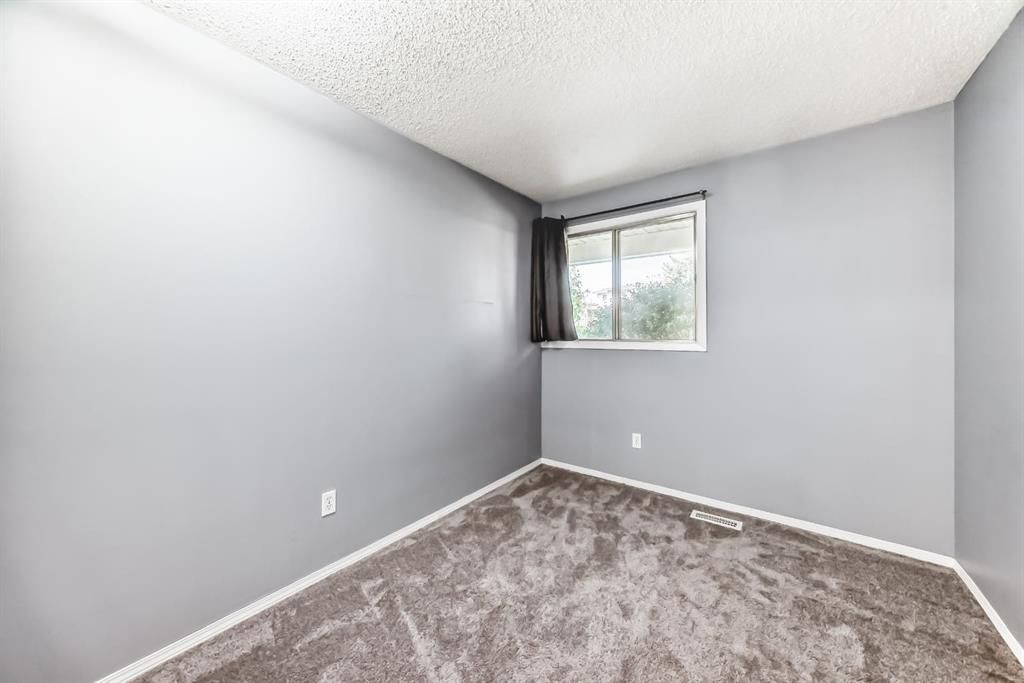 Empty gray bedroom with carpet and a small window letting in daylight