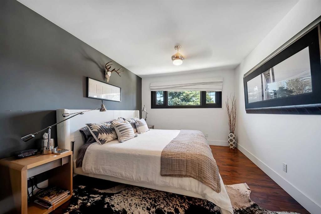 Modern bedroom with bed, wooden floor, gray walls, and a large window letting in natural light