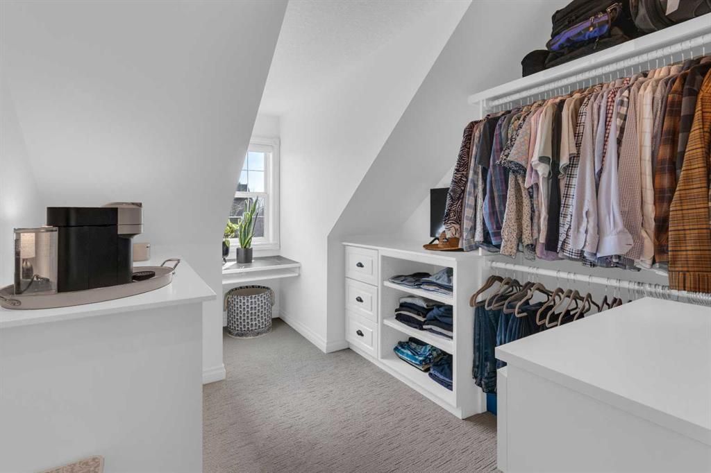 Bright walk-in closet with hanging clothes, shelves, drawers, and a window seat at the far end.