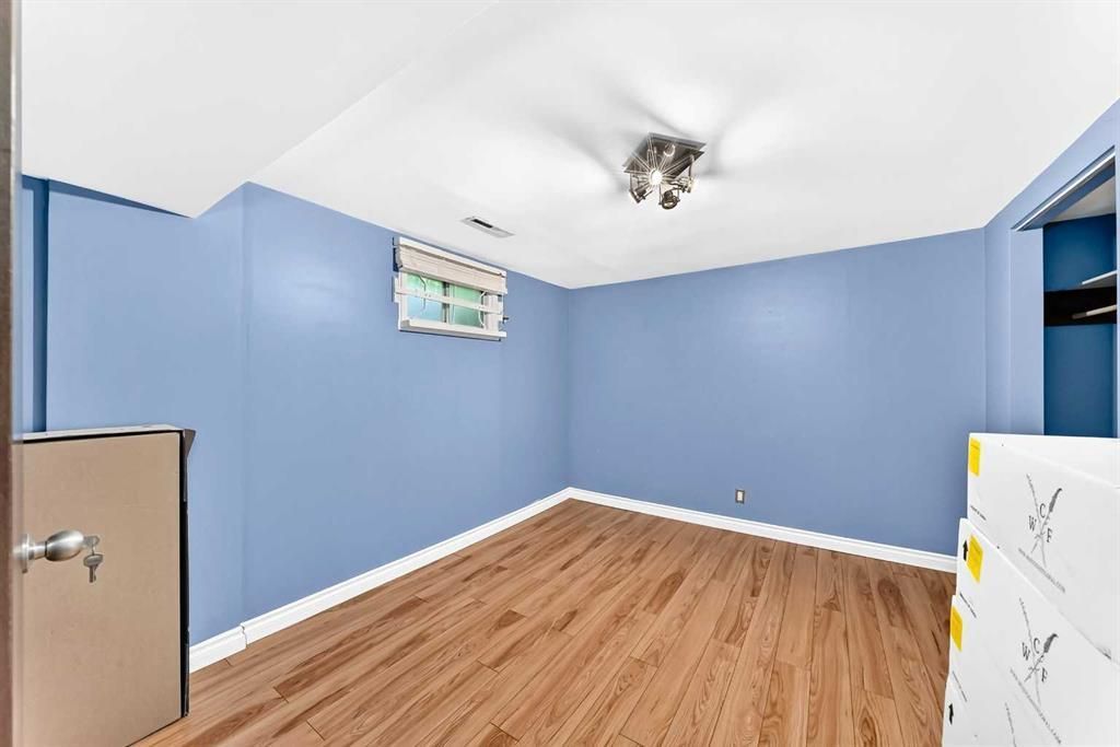 Empty blue room with wood floor, small window, and a ceiling light fixture