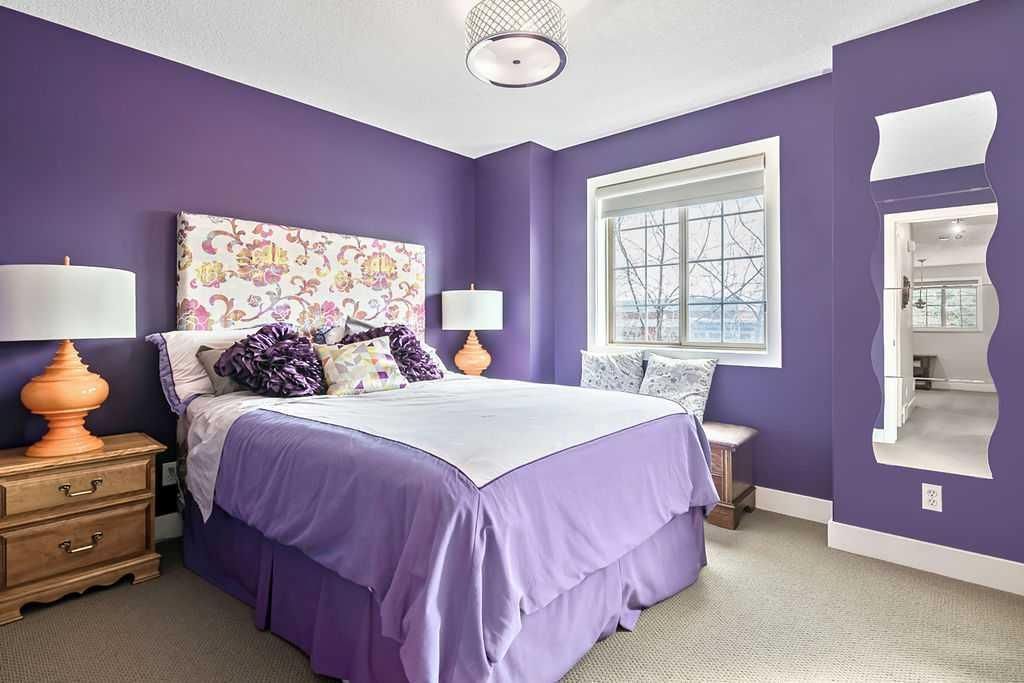 Purple bedroom with a white bed, floral headboard, bedside lamps, and a window with natural light