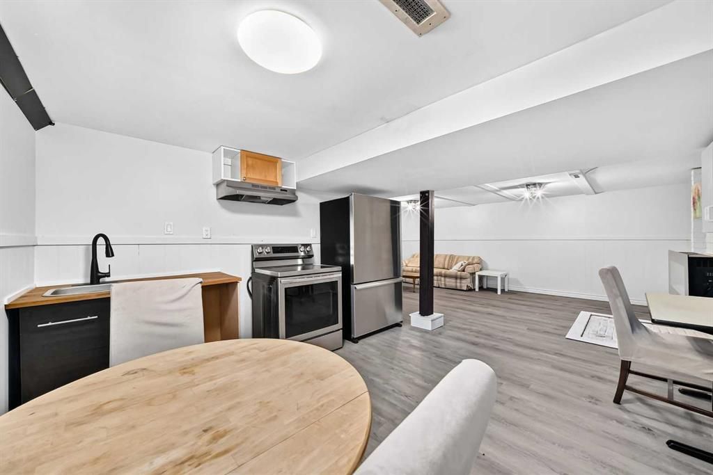 Bright modern kitchen and living area with stainless appliances, white walls, and gray flooring