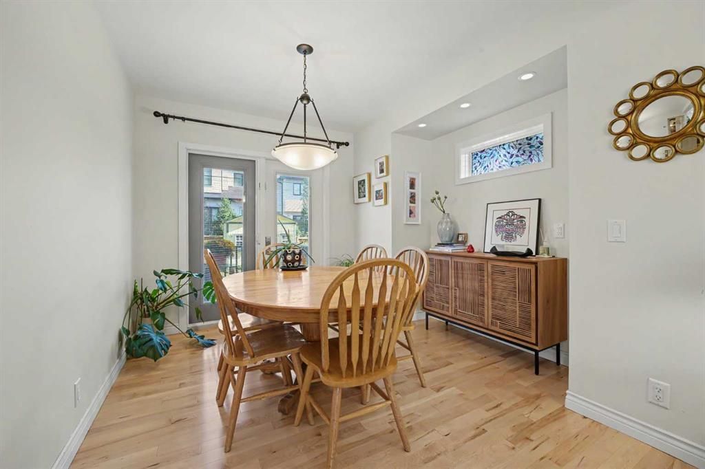 Bright dining room with wooden table, chairs, sideboard, and large windows on light wood floors