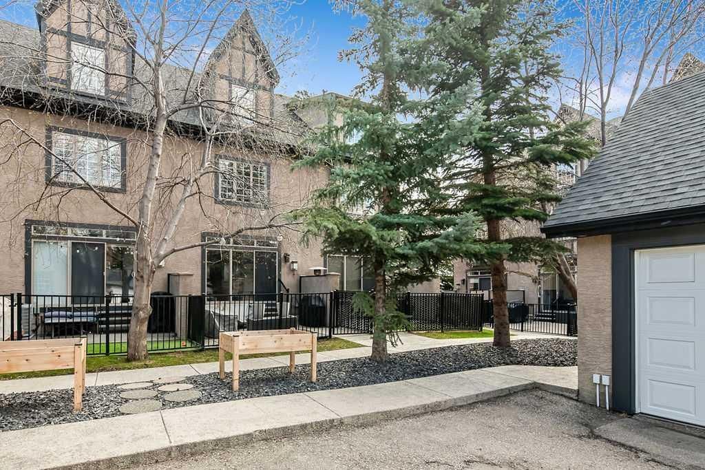 Courtyard of beige townhouses with black fences, benches, trees, and a gray shed roof at right