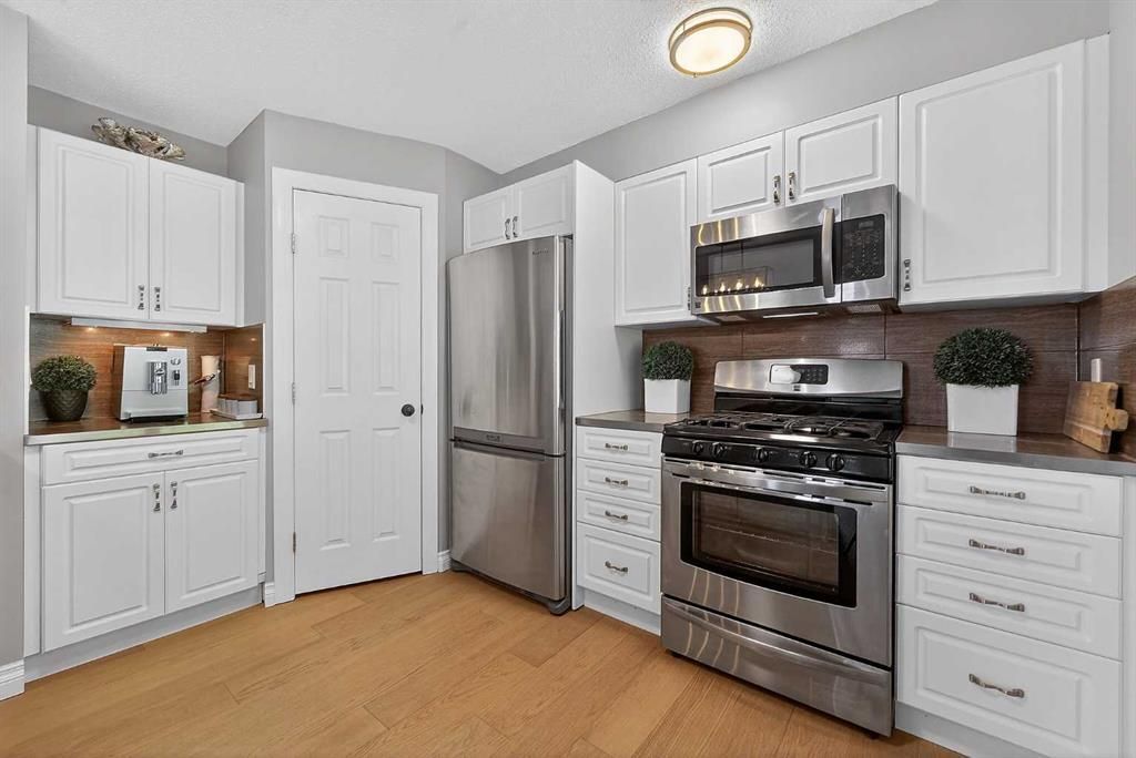 Bright modern kitchen with stainless steel appliances, white cabinets, and light wood floors