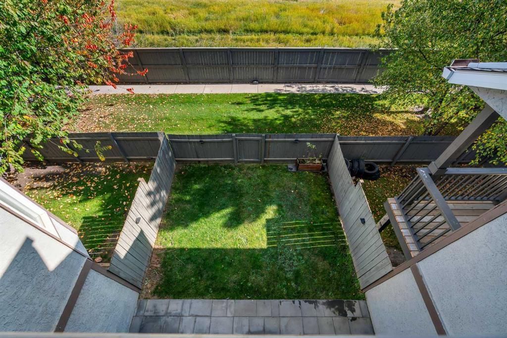 Backyard view of a small lawn, stone steps, and wooden fences leading to a street beyond