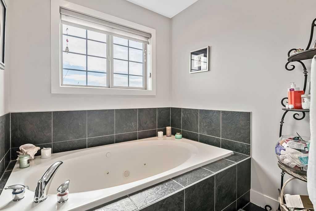 Modern bathroom with a white tub, dark tile surround, and a window above it