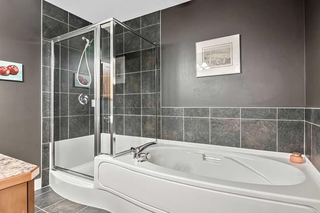 Modern bathroom with glass shower, white soaking tub, and gray tile walls