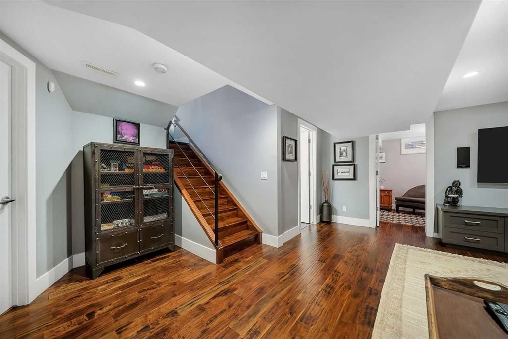 Modern living room with hardwood floors, staircase, glass cabinet, and TV area