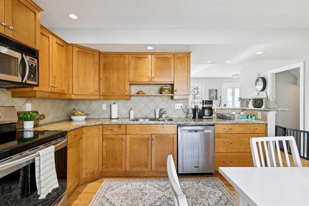 Bright kitchen with wooden cabinets, stainless dishwasher, stove, and dining table in foreground
