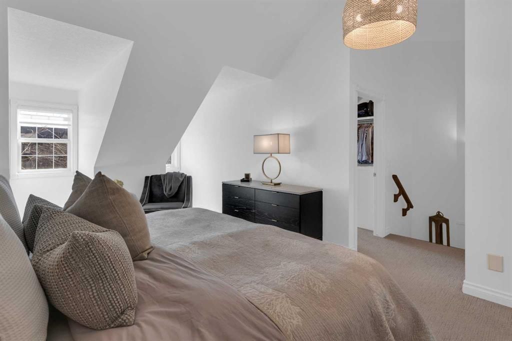 Bright bedroom with a bed, dresser, lamp, and slanted white ceilings