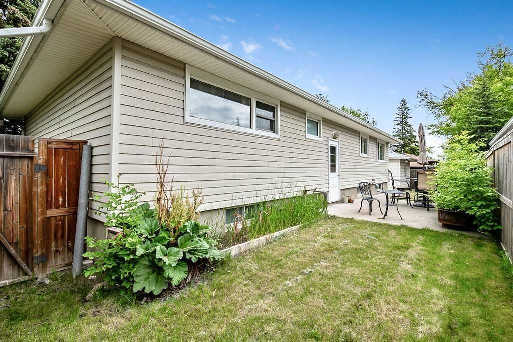 Side yard with beige house, small patio table, and green lawn under a bright blue sky