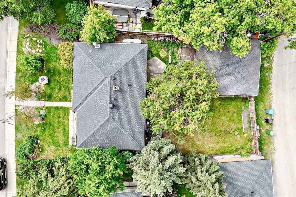 Aerial view of two houses with gray roofs, trees, and lawns in a residential neighborhood.
