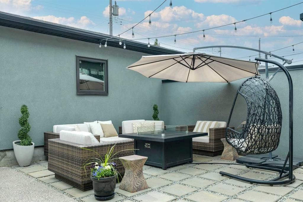 Rooftop patio with wicker sofa, dining table, hanging chair, umbrella, and potted plants under a blue sky.