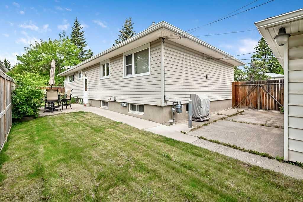 Backyard with green lawn, white house siding, concrete path, and patio furniture under a blue sky