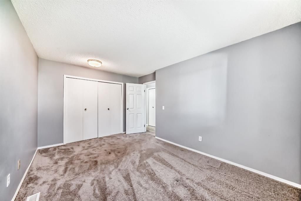 Empty gray bedroom with carpet, closet doors, and a ceiling light