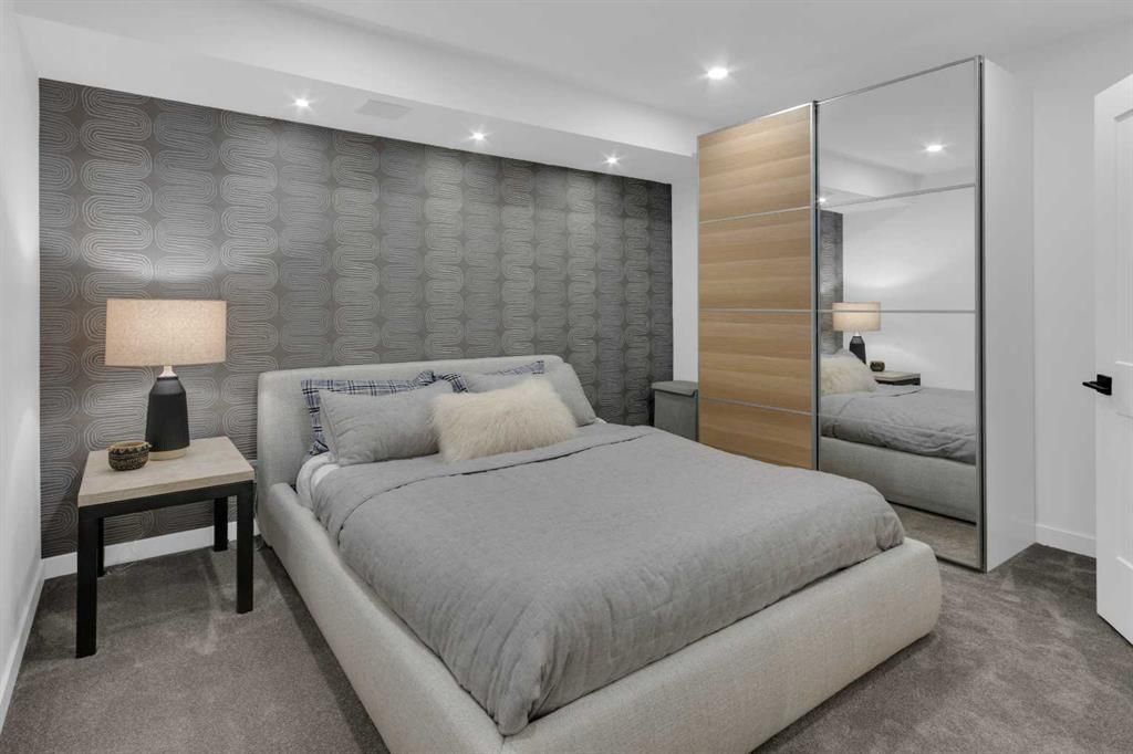 Modern bedroom with a gray bed, nightstand lamp, textured accent wall, and mirrored wardrobe.