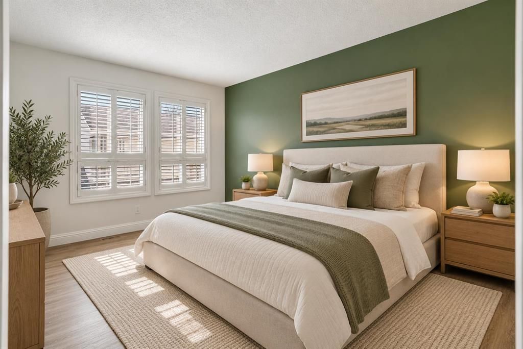 Neatly made bed in a bedroom with green accent wall, bedside lamps, and window shutters