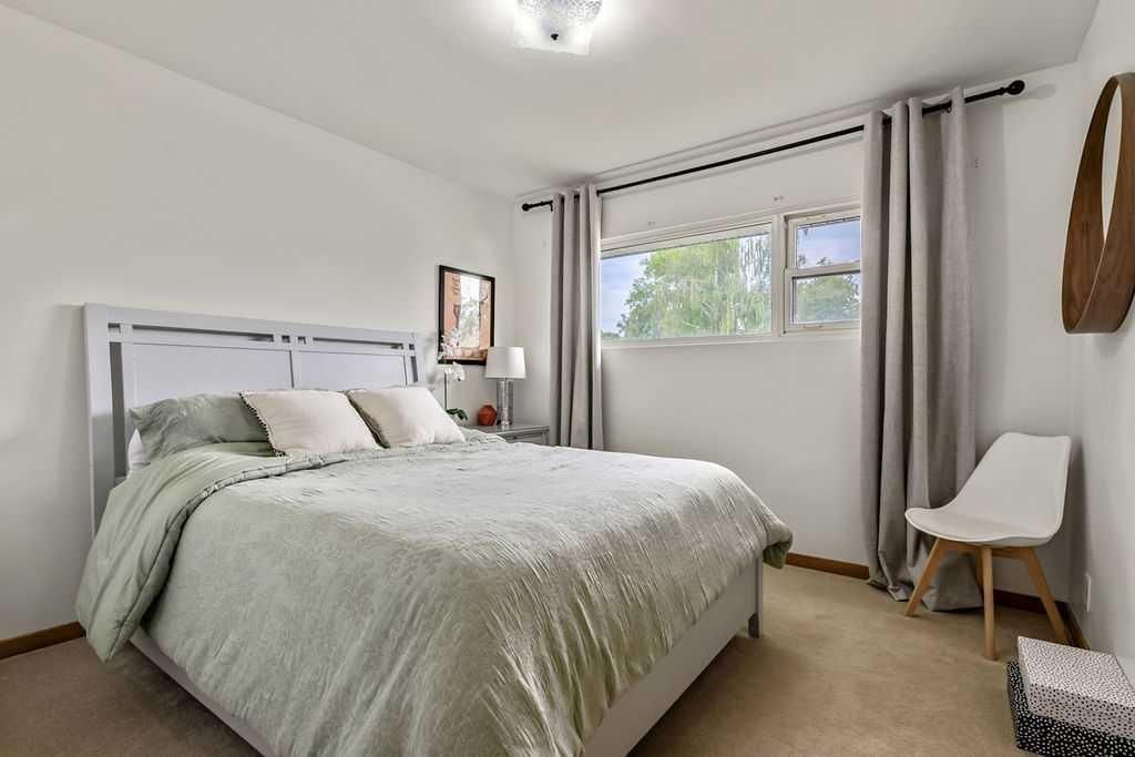 Bright bedroom with a bed, light gray curtains, window, and a chair by the wall.