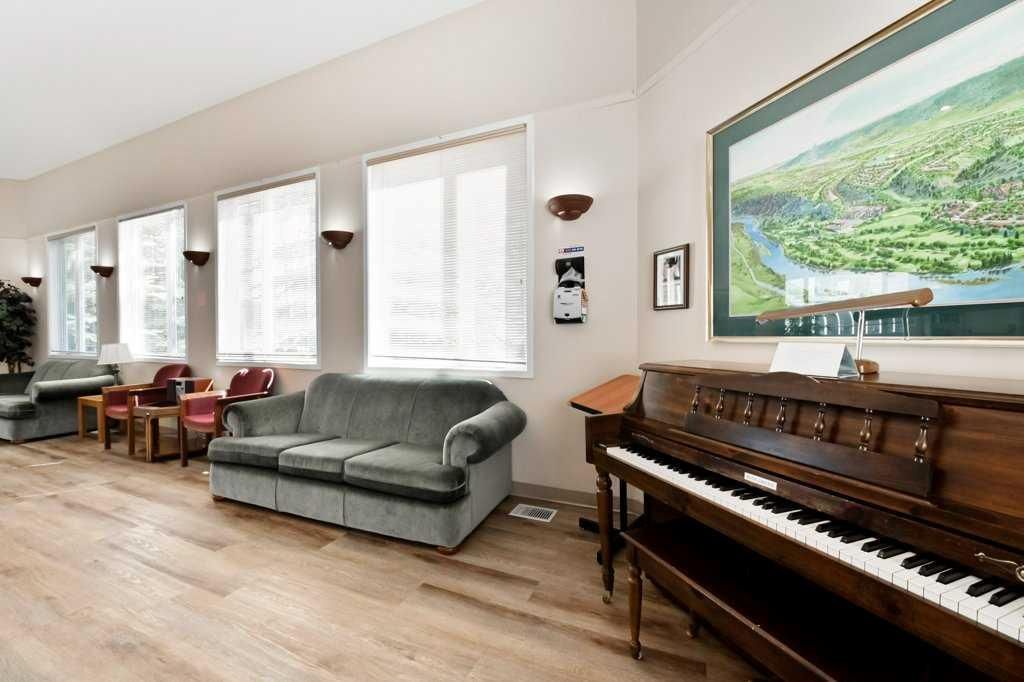 Bright living room with large windows, gray sofa, chairs, and a wooden piano beside a landscape painting