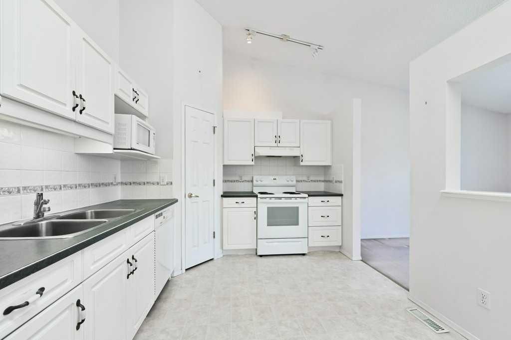 Bright white galley kitchen with white cabinets, black countertops, stove, and microwave
