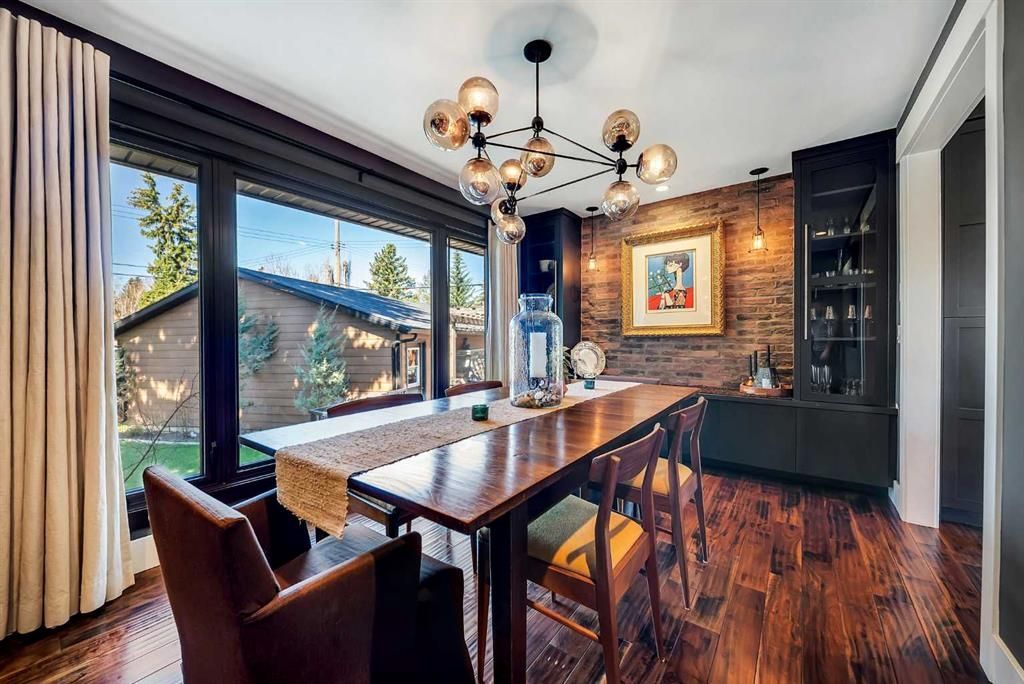 Modern dining room with a long wooden table, dark chairs, chandelier, and large windows overlooking greenery