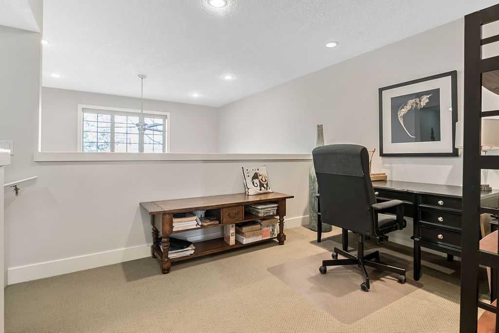 Modern home office with desk, black chair, wall art, and a small window over carpeted flooring