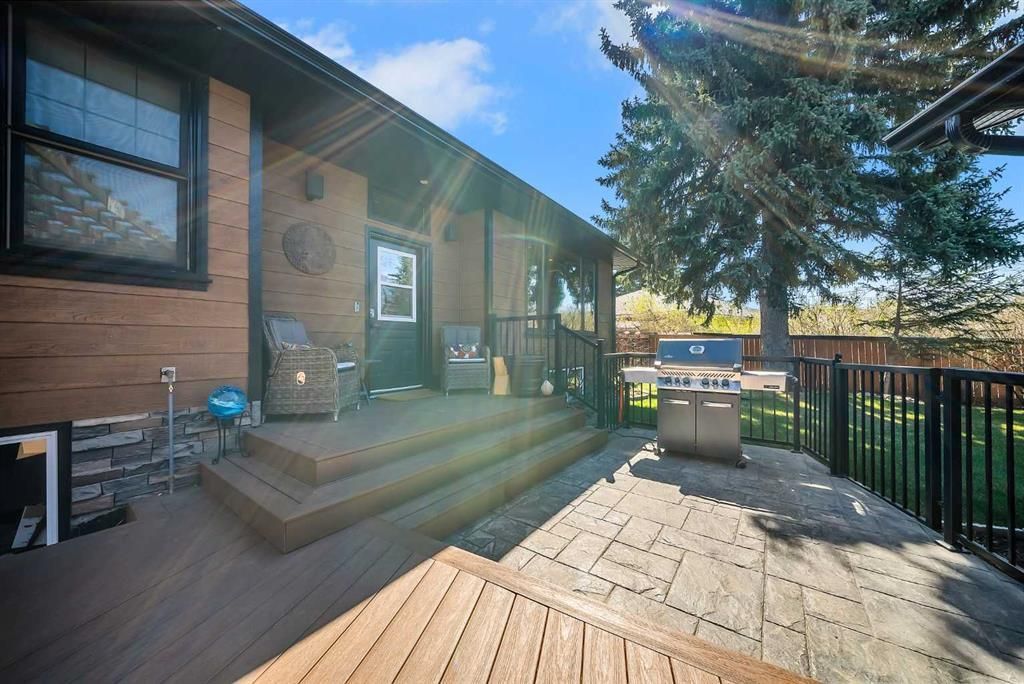 Wood-sided house deck with steps, patio pavers, and a fenced yard under a large tree.