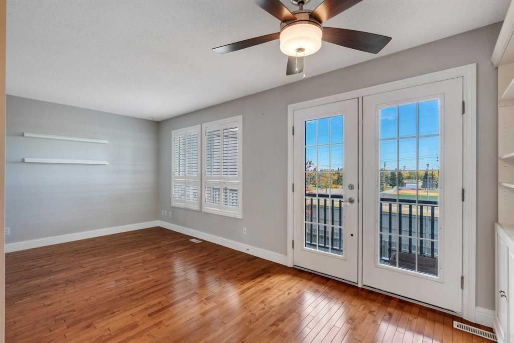 Bright empty room with hardwood floors, gray walls, ceiling fan, and French doors with white shutters