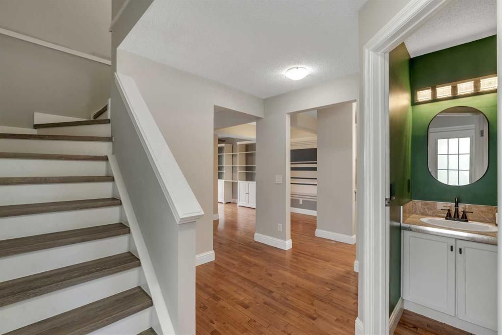 Bright hallway with staircase, hardwood floors, and a bathroom vanity with green wall accents