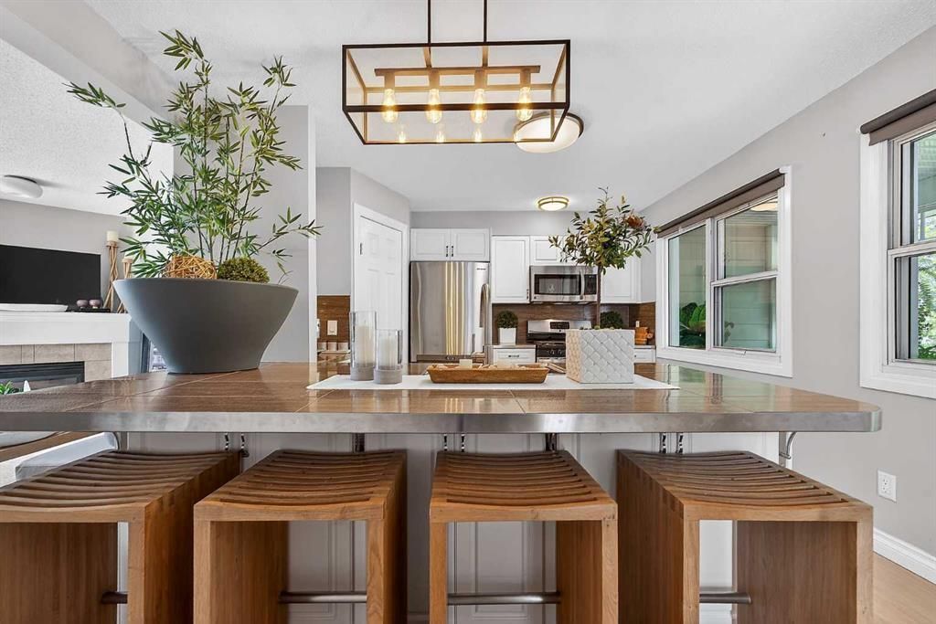 Modern kitchen with large island, wooden stools, pendant light, and bright windows looking outside