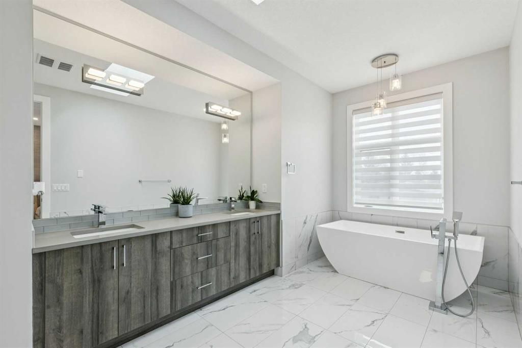 Modern bathroom with double vanity, large mirror, freestanding tub, and bright white tile flooring