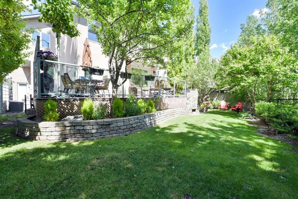 Sunny backyard with green lawn, stone retaining wall, and a house with patio and trees