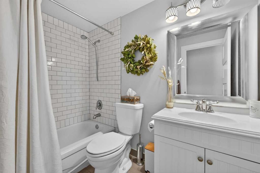 Bright white bathroom with tub, toilet, vanity, mirror, and green wreath decor
