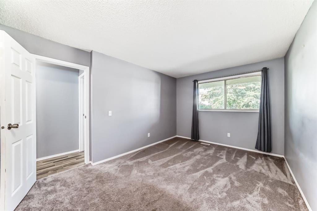 Empty gray bedroom with carpet, white door, and a window with dark curtains