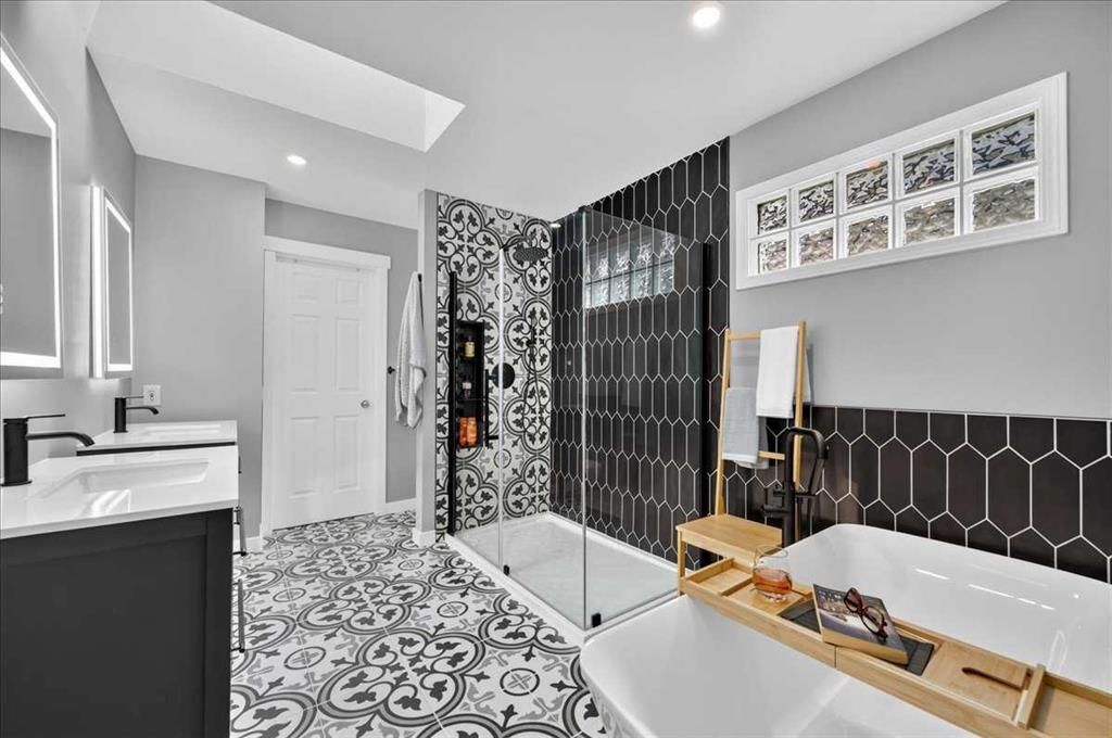 Modern bathroom with black hex tile, glass shower, freestanding tub, and patterned floor tiles