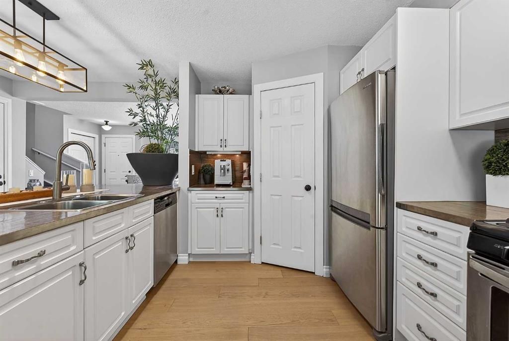 Bright modern kitchen with white cabinets, stainless fridge, wood floors, and a large sink window
