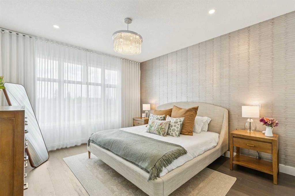 Bright, airy bedroom with a beige bed, wooden nightstand, chandelier, and sheer white curtains