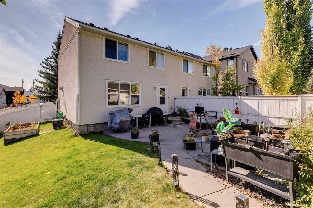 Backyard patio and lawn beside a beige two-story house, with outdoor furniture and potted plants.