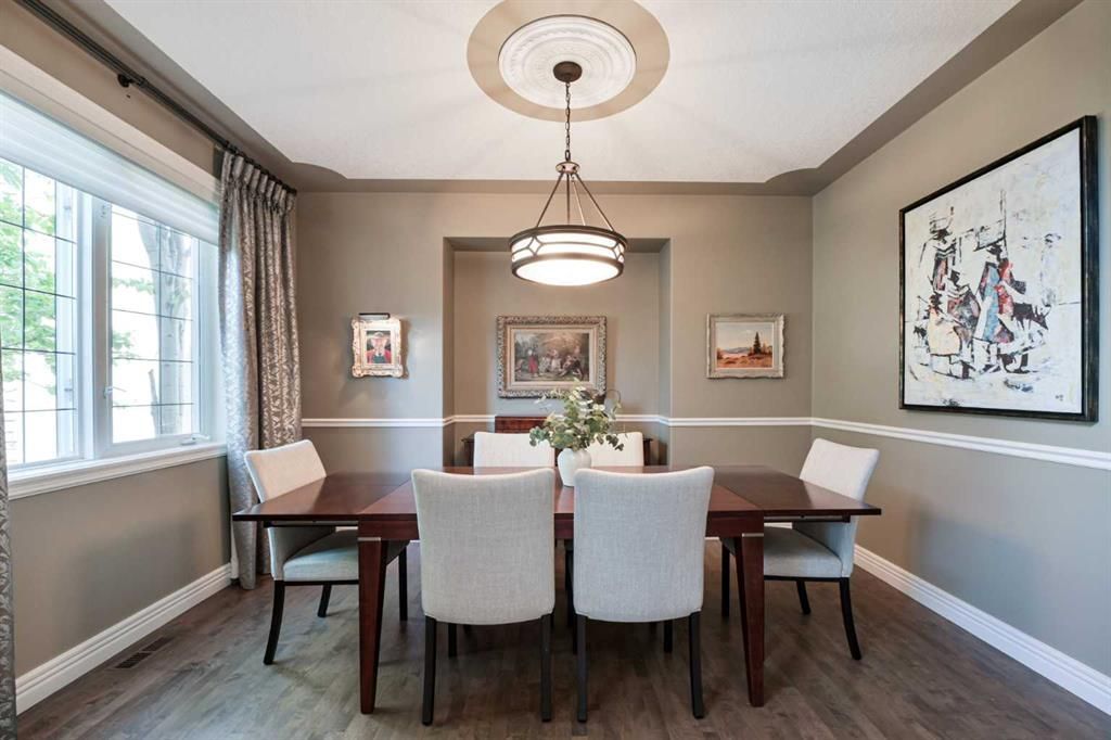 Bright dining room with a wooden table, upholstered chairs, large windows, and framed wall art.