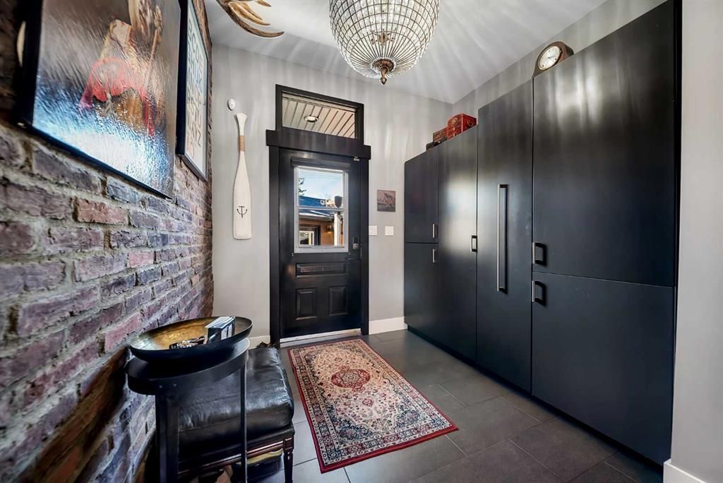 Narrow hallway with dark built-in cabinets, brick accent wall, chandelier, and front door with rug