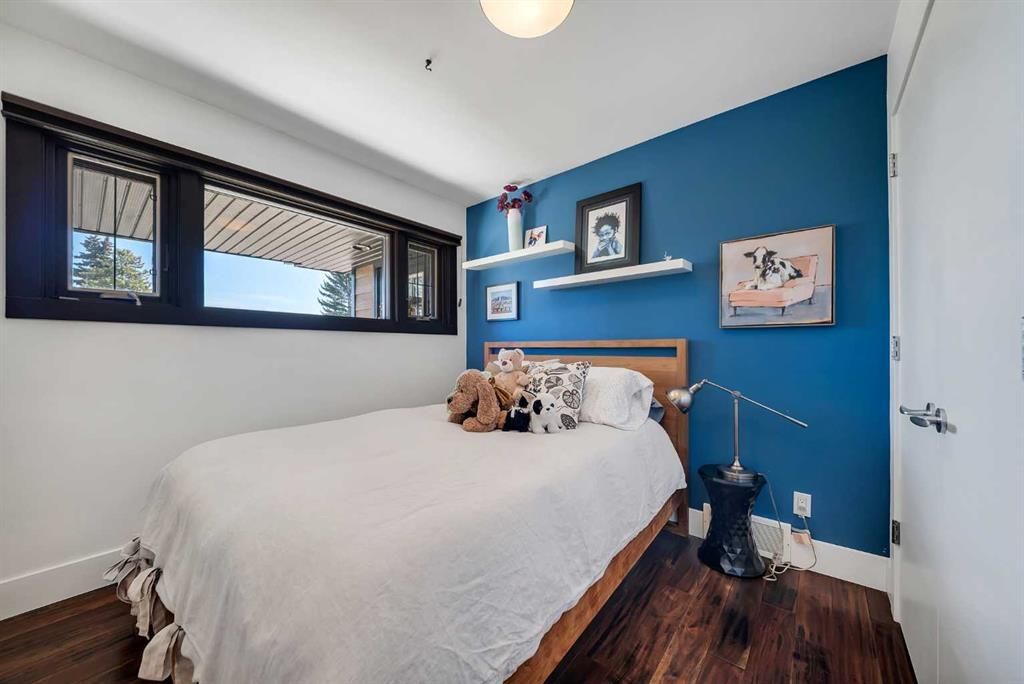 Bright bedroom with blue accent wall, white bed, dark wood floor, and narrow windows.