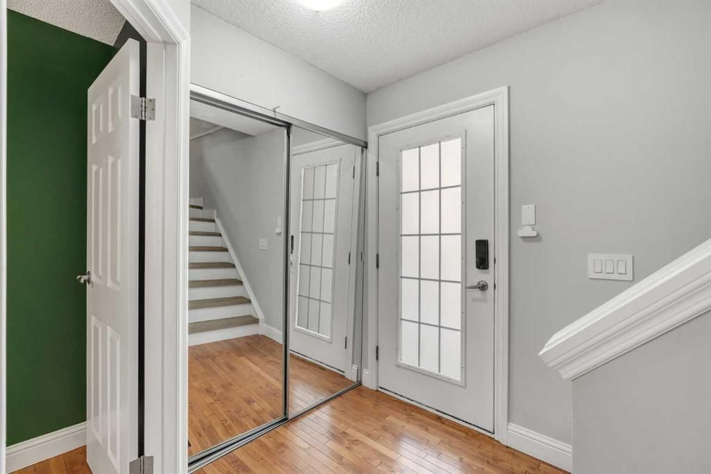 Entryway with white front door, mirrored closet, wood floor, and staircase beside a green wall