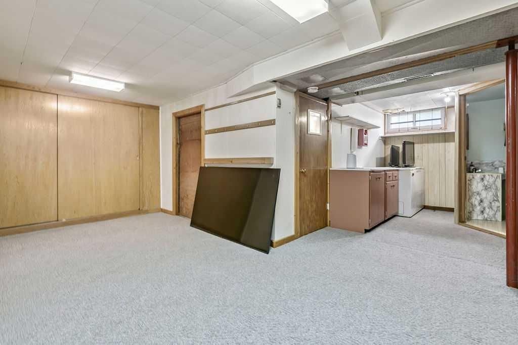 Empty basement room with carpet, wood paneling, and a small kitchenette area