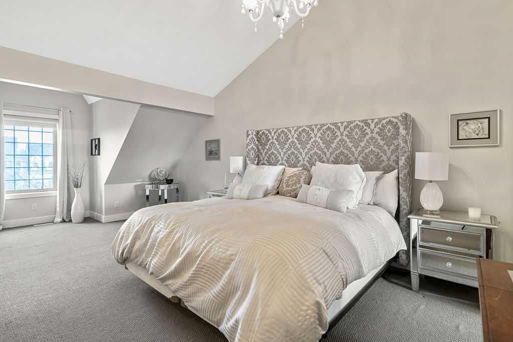 Bright bedroom with a large bed, mirrored nightstand, chandelier, and gray carpet and walls