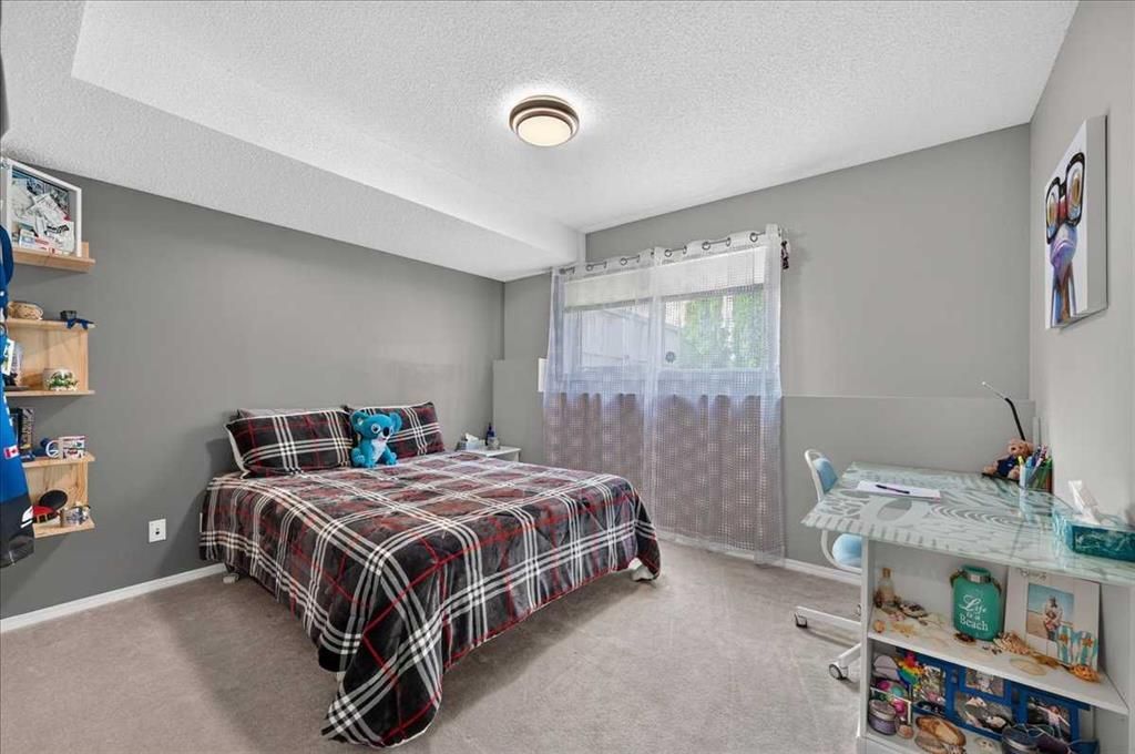 Small bedroom with a plaid bedspread, gray walls, and a window with sheer curtains