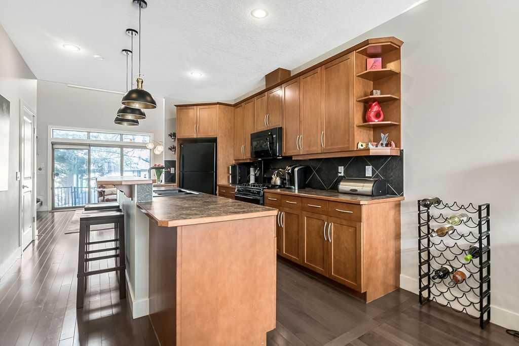 Modern kitchen with wood cabinets, island counter, bar stools, and dark flooring, open to a bright dining area