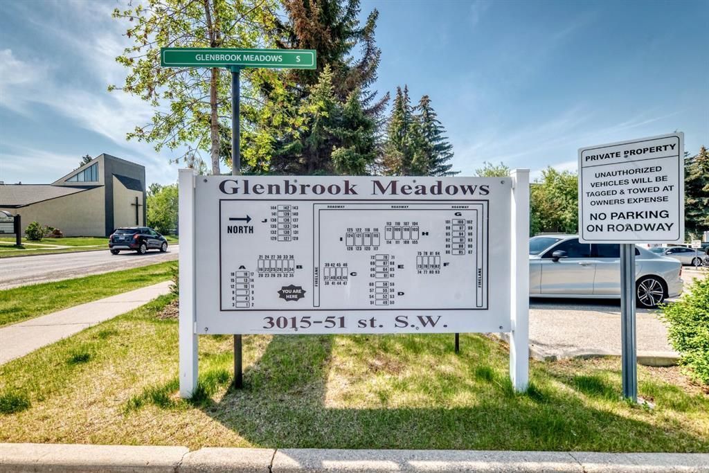 Glencoe Meadows entrance sign beside a sidewalk and parked car on a sunny day