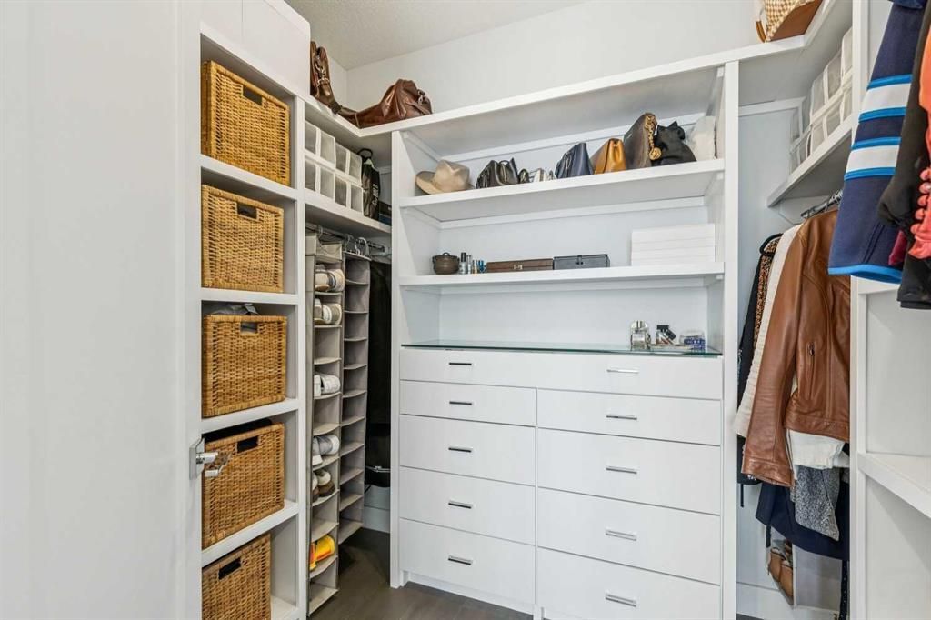 Walk-in closet with white shelves, drawers, hanging clothes, and woven baskets