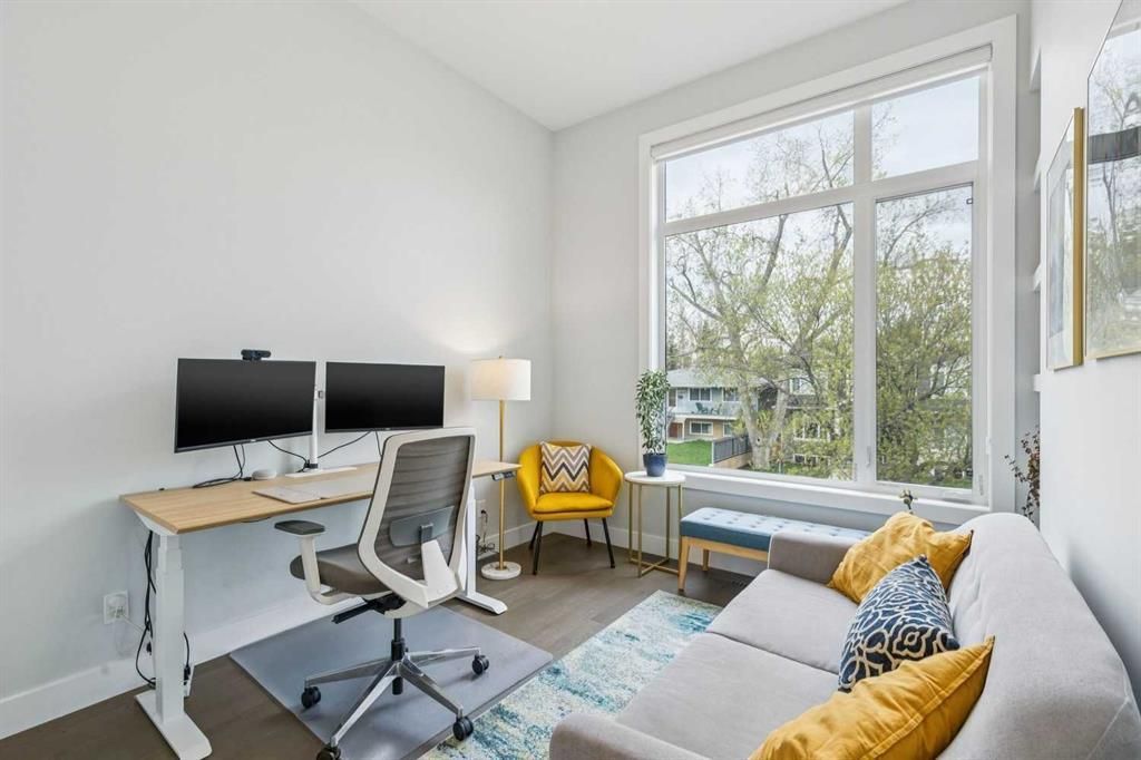 Bright home office with desk, dual monitors, gray chair, sofa, yellow accent chair, and large window.